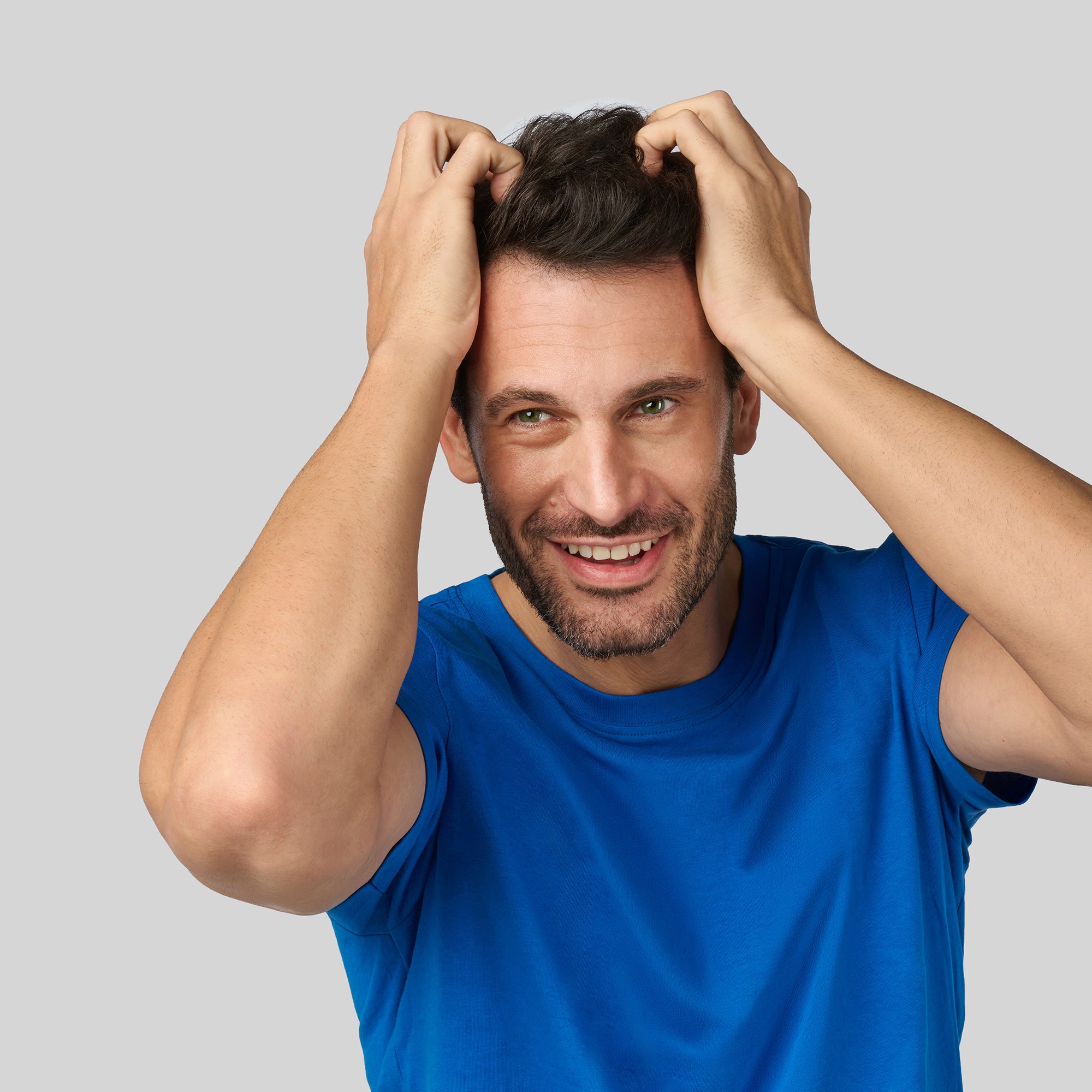 Primo piano di un uomo con capelli corti e scuri che si tocca i capelli con entrambe le mani