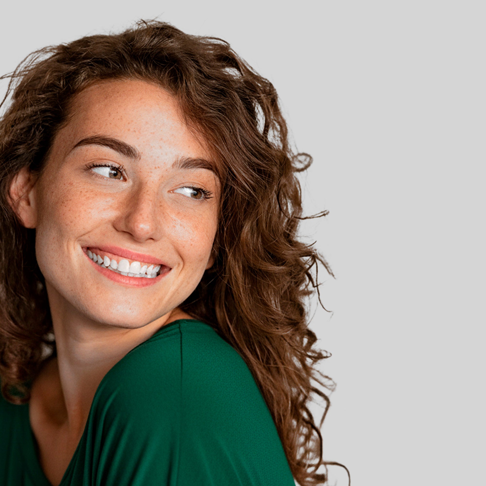 Primo piano di donna sorridente con capelli ricci, simbolo di cura e salute della chioma grazie a soluzioni mirate per ogni esigenza dei capelli