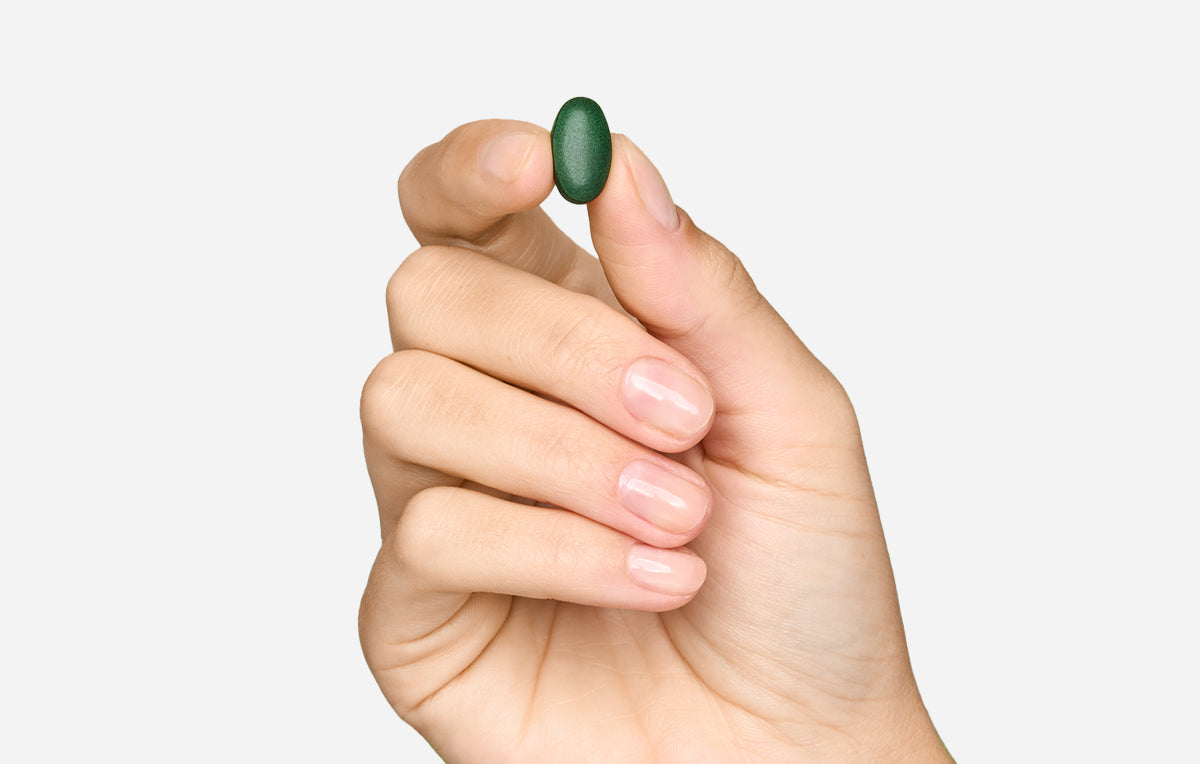 Mano che tiene una compressa verde Bioscalin®: integratore alimentare per il benessere dei capelli