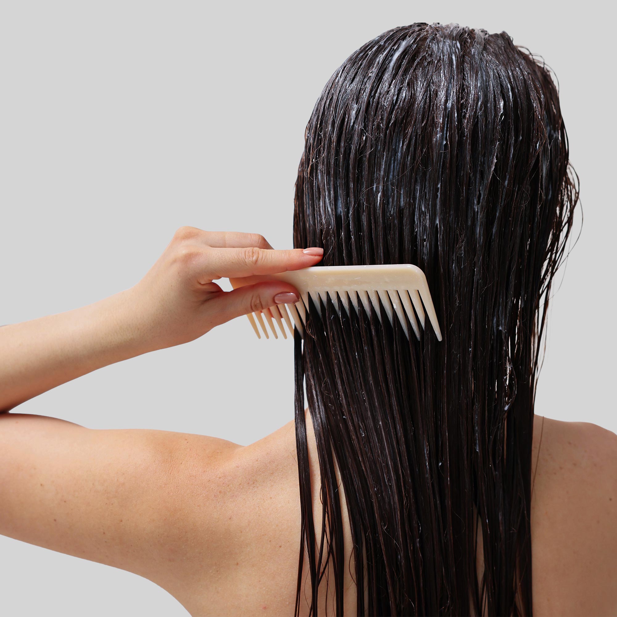 Donna che si pettina i capelli, con prodotto applicato sulla chioma, vista da dietro