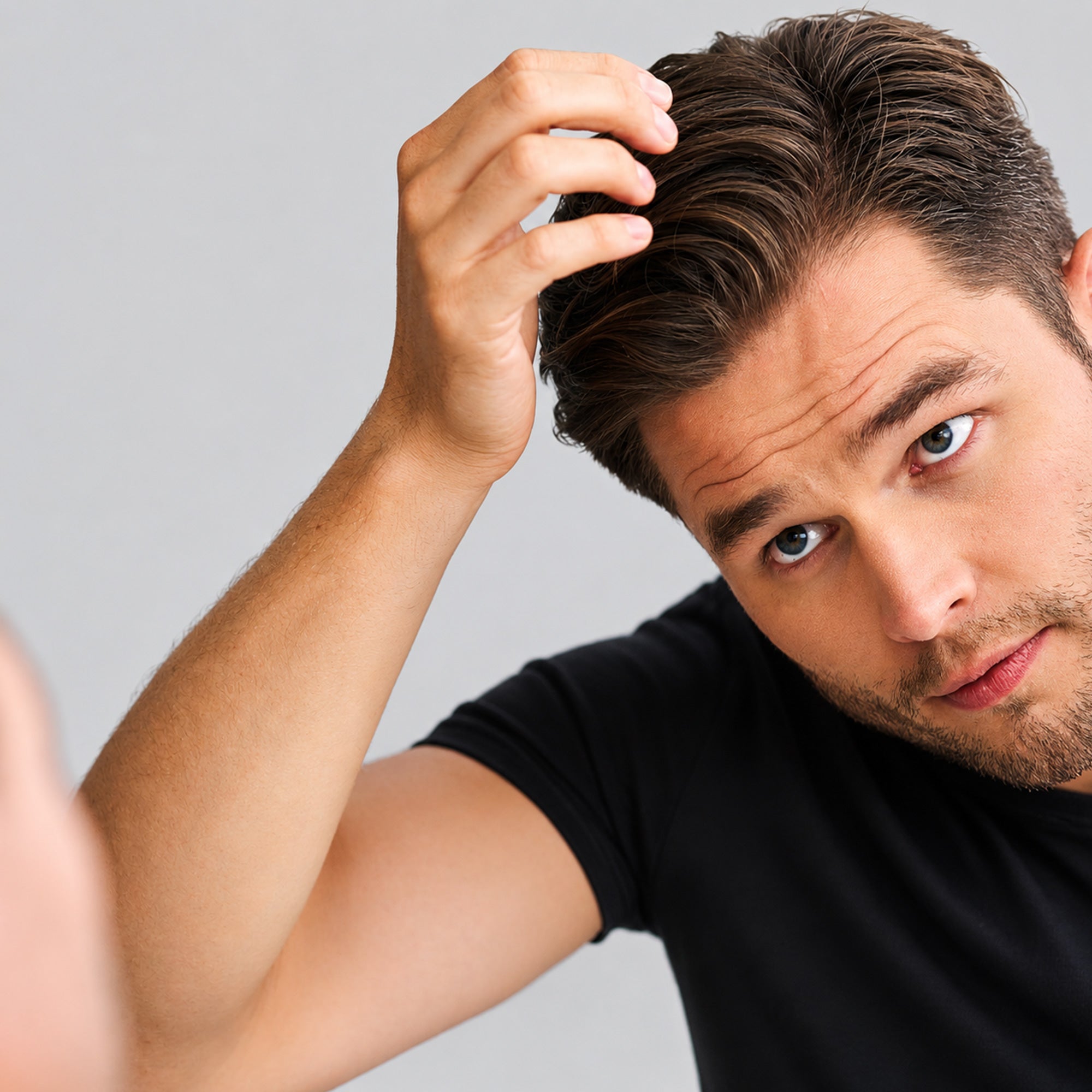 Uomo con capelli biondi scuri corti, volto leggermente inclinato, che si pettina i capelli con la mano