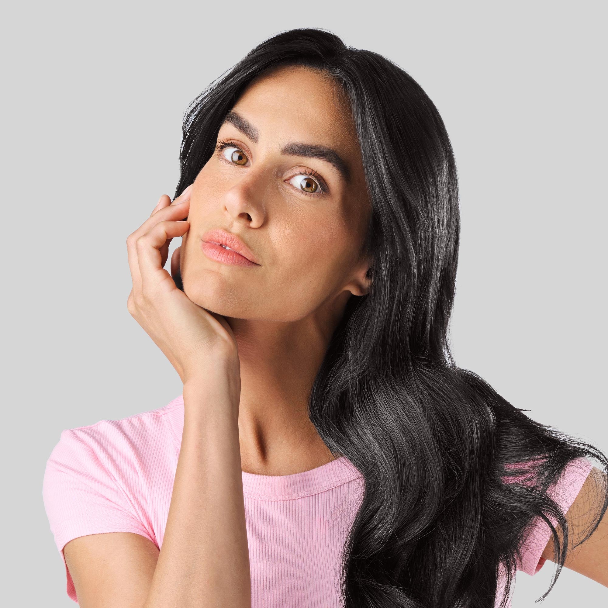 Donna con lunghi capelli neri, folti e luminosi, che posa con una mano appoggiata delicatamente al viso.
