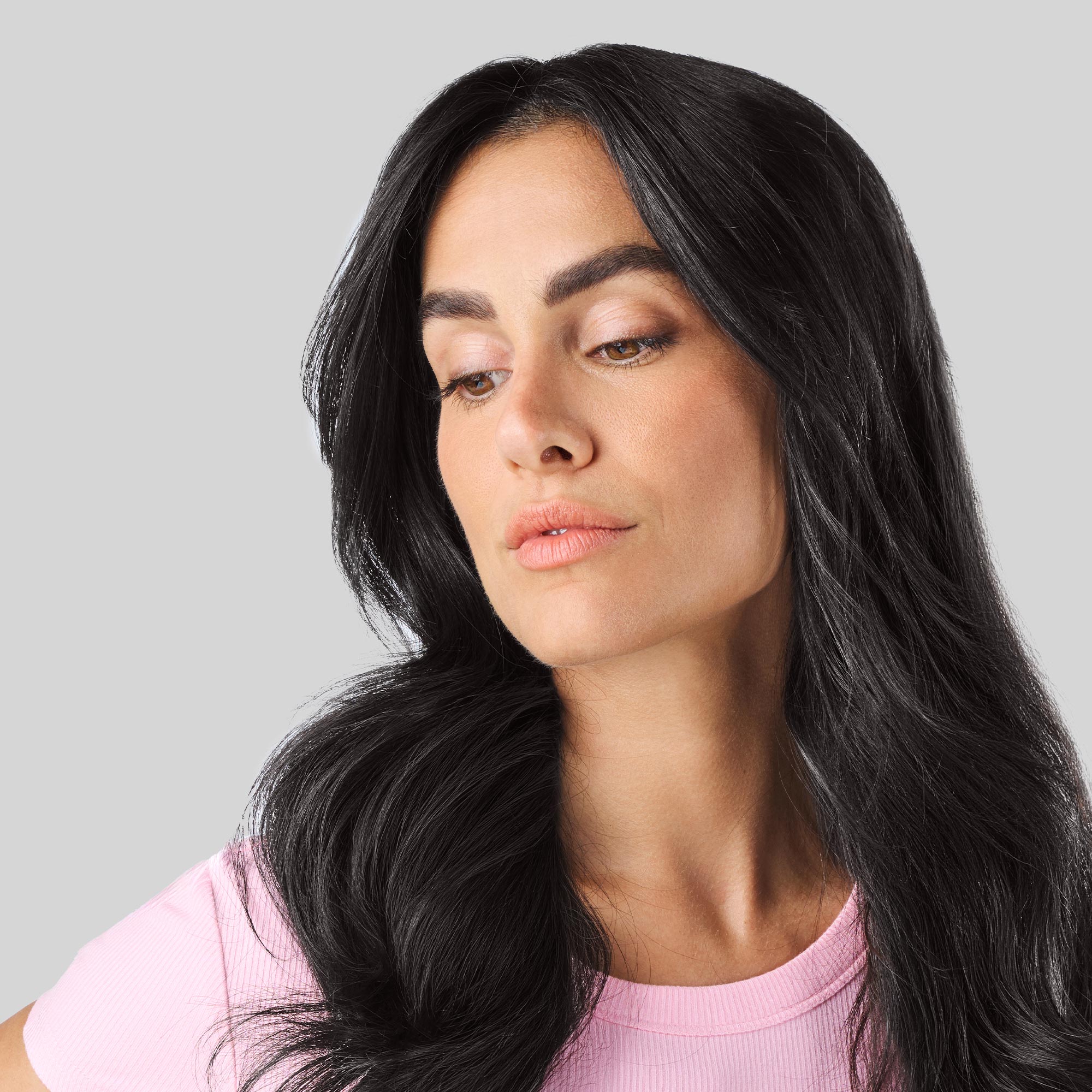 Primo piano di una donna con lunghi capelli neri, folti e luminosi, che guarda verso il basso.