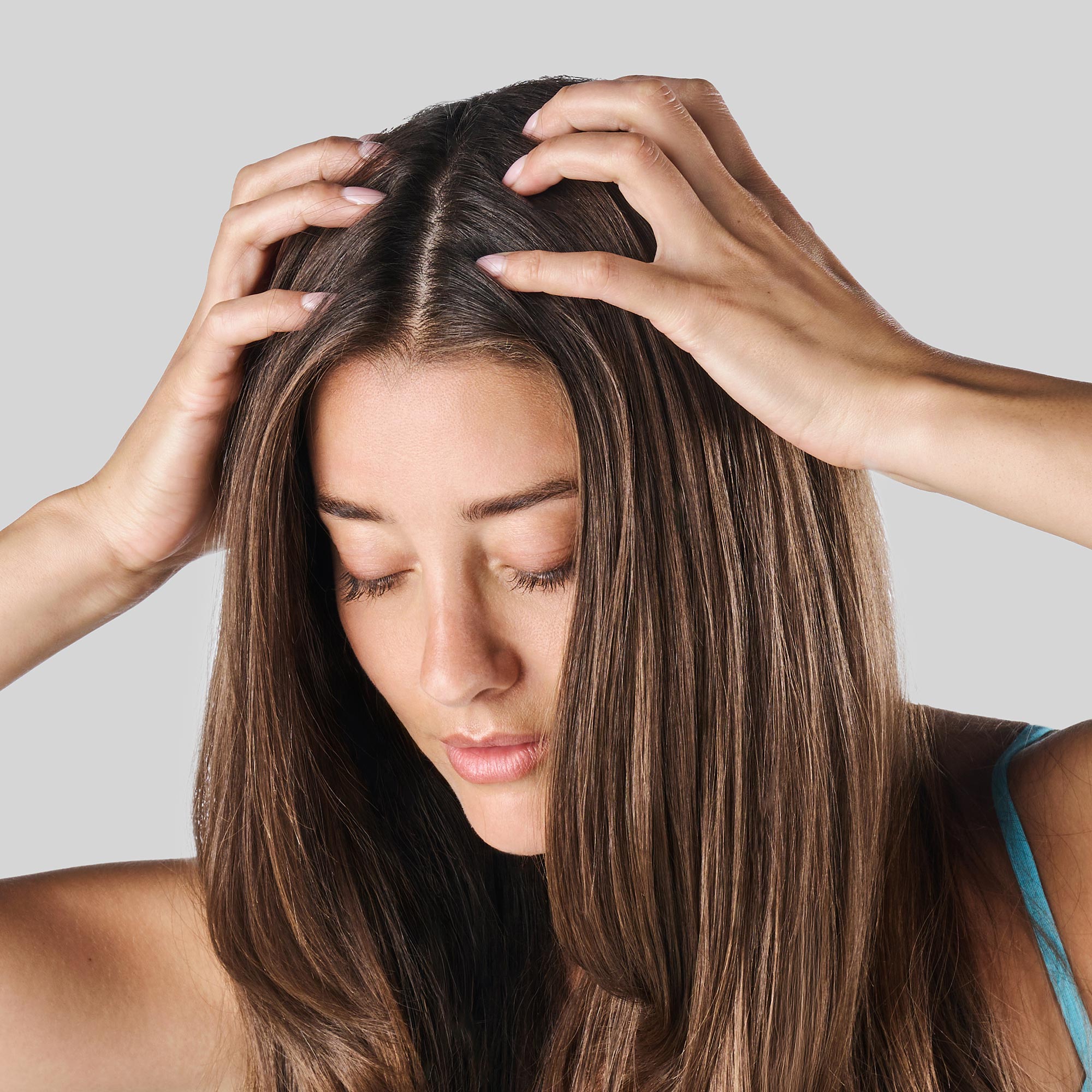 Donna con capelli lunghi e lisci che massaggia il cuoio capelluto con entrambe le mani.