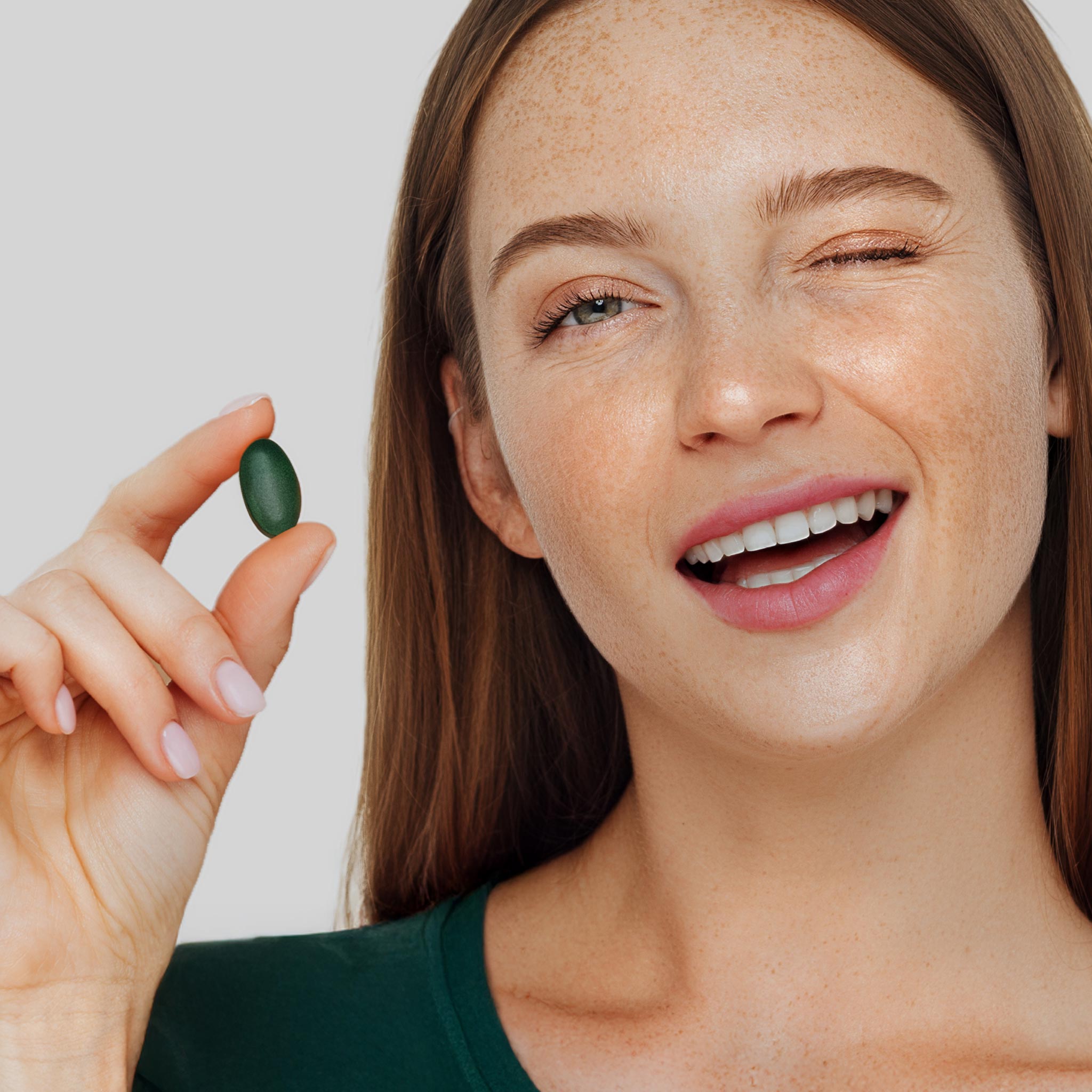 Modella sorridente mostra una compressa Bioscalin®, il gesto quotidiano per il benessere dei tuoi capelli