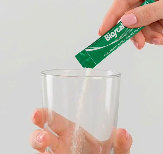 Una mano versa la bustina di Bioscalin® TOTAL•CARE in un bicchiere di vetro