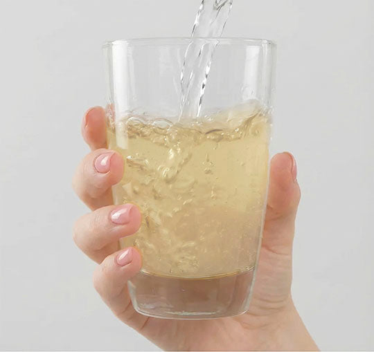 Dettaglio di una mano che sorregge il bicchiere contenente una bustina di Bioscalin® TOTAL•CARE in cui viene versata dell'acqua