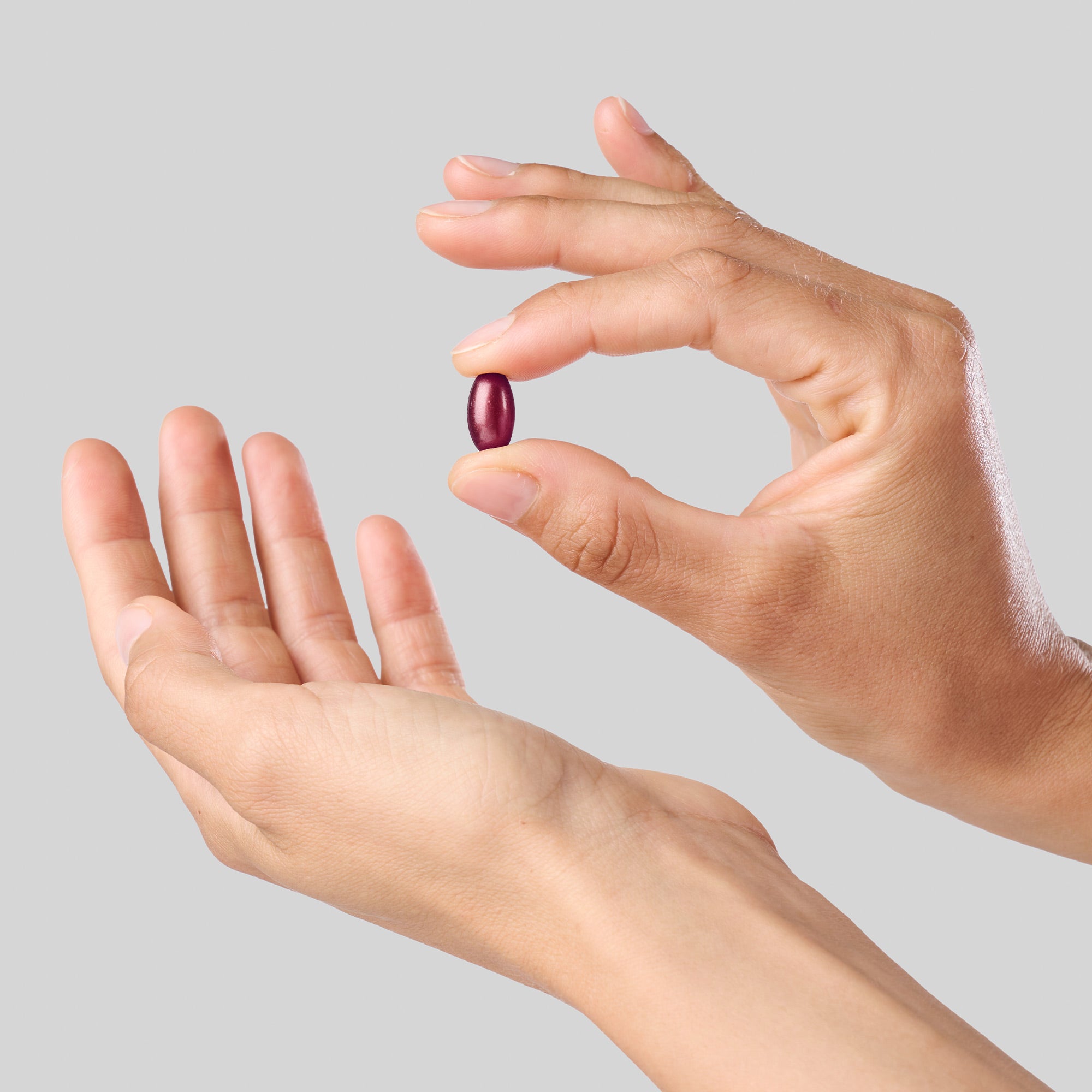 Dettaglio di una capsula softgel di Bioscalin® Post•Partum tenuta tra le dita, con una seconda mano aperta sotto.
