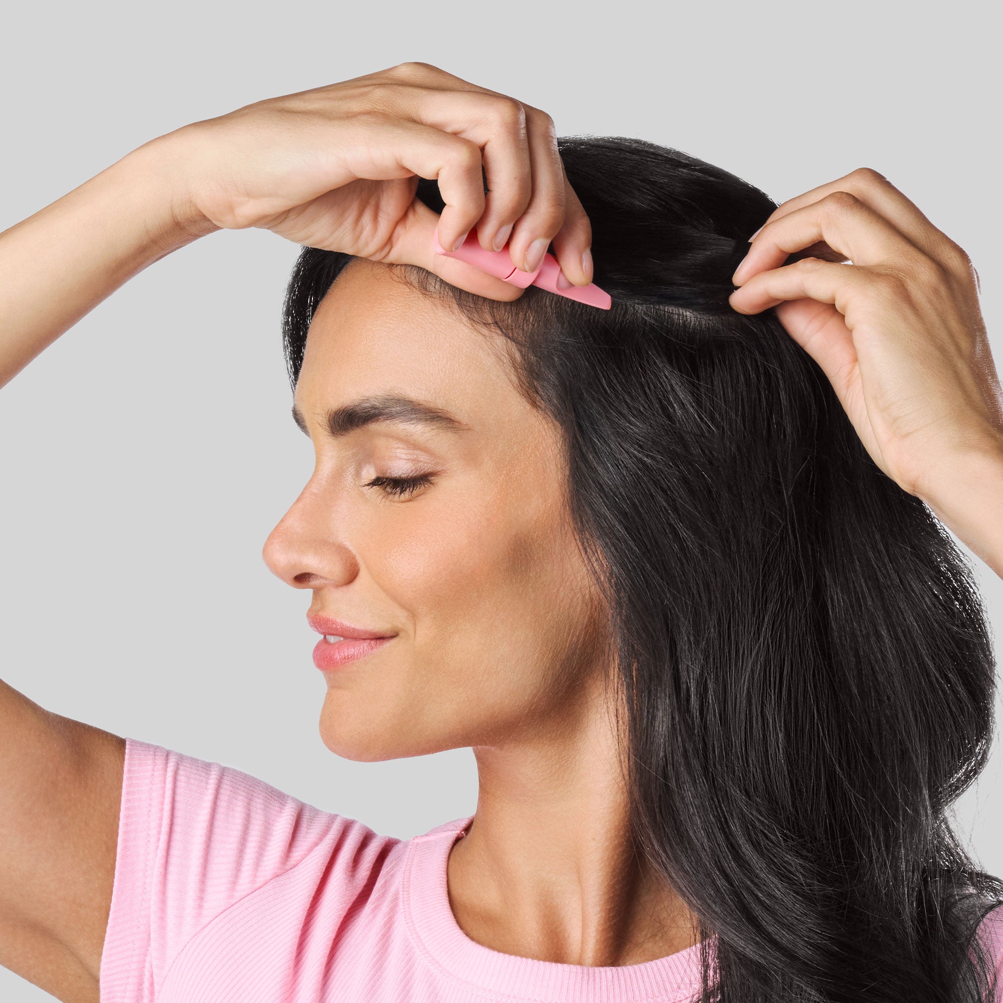 Donna con lunghi capelli neri che applica Bioscalin® Post•Partum Booster Capillare direttamente sul cuoio capelluto, separando i capelli per facilitare l’applicazione.