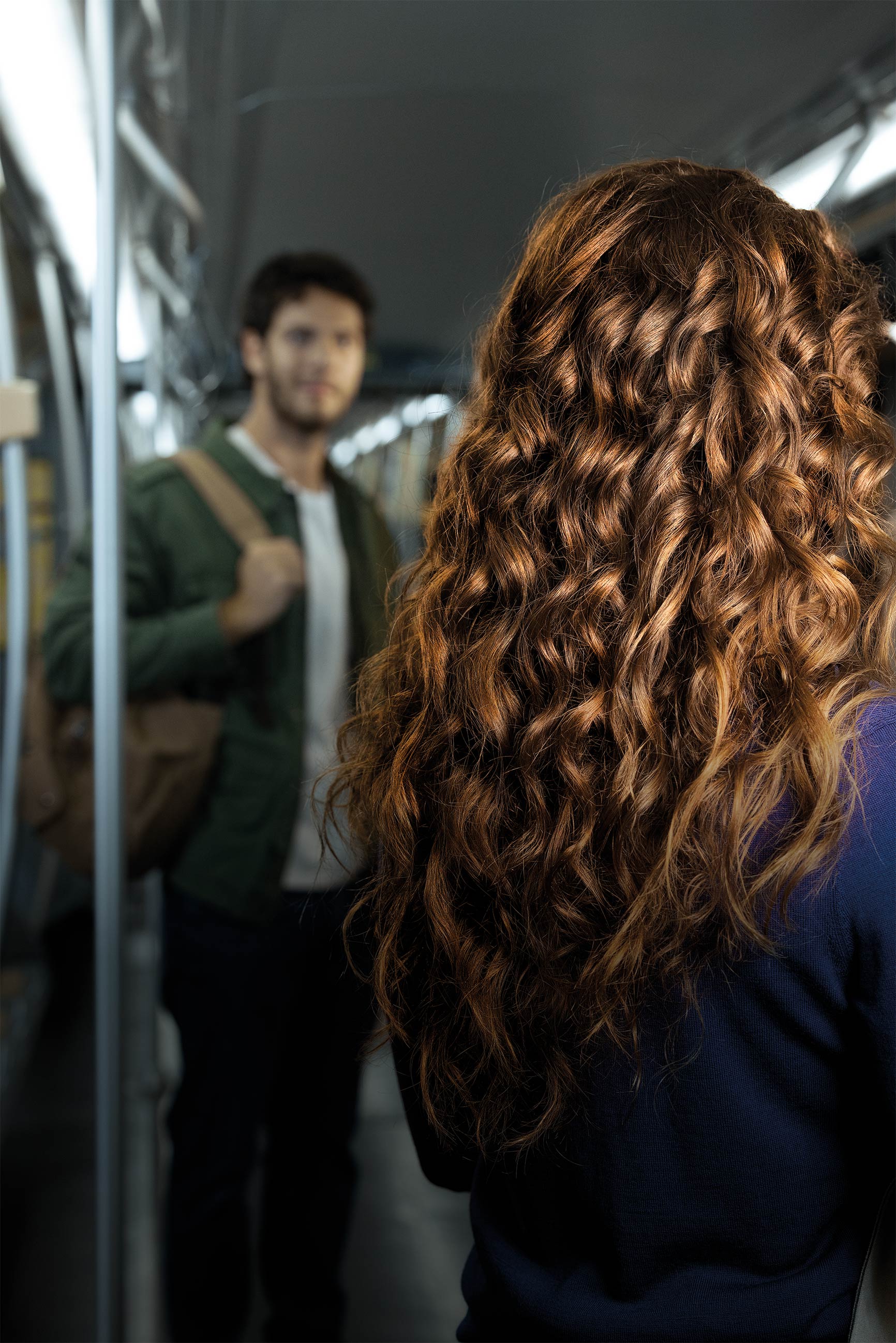 Donna con lunghi capelli ricci, voluminosi e luminosi all’interno di un vagone della metropolitana.