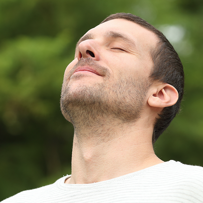 Uomo con capelli molto corti che respira felice con la testa rivolta verso il cielo e gli occhi chiusi 