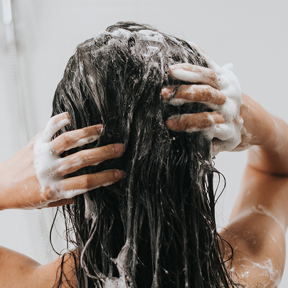Donna che massaggia i suoi capelli neri con lo shampoo 