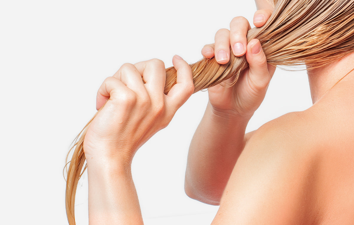 Mano che accarezza una ciocca di capelli castano chiaro: sani e nutriti con i trattamenti Bioscalin®
