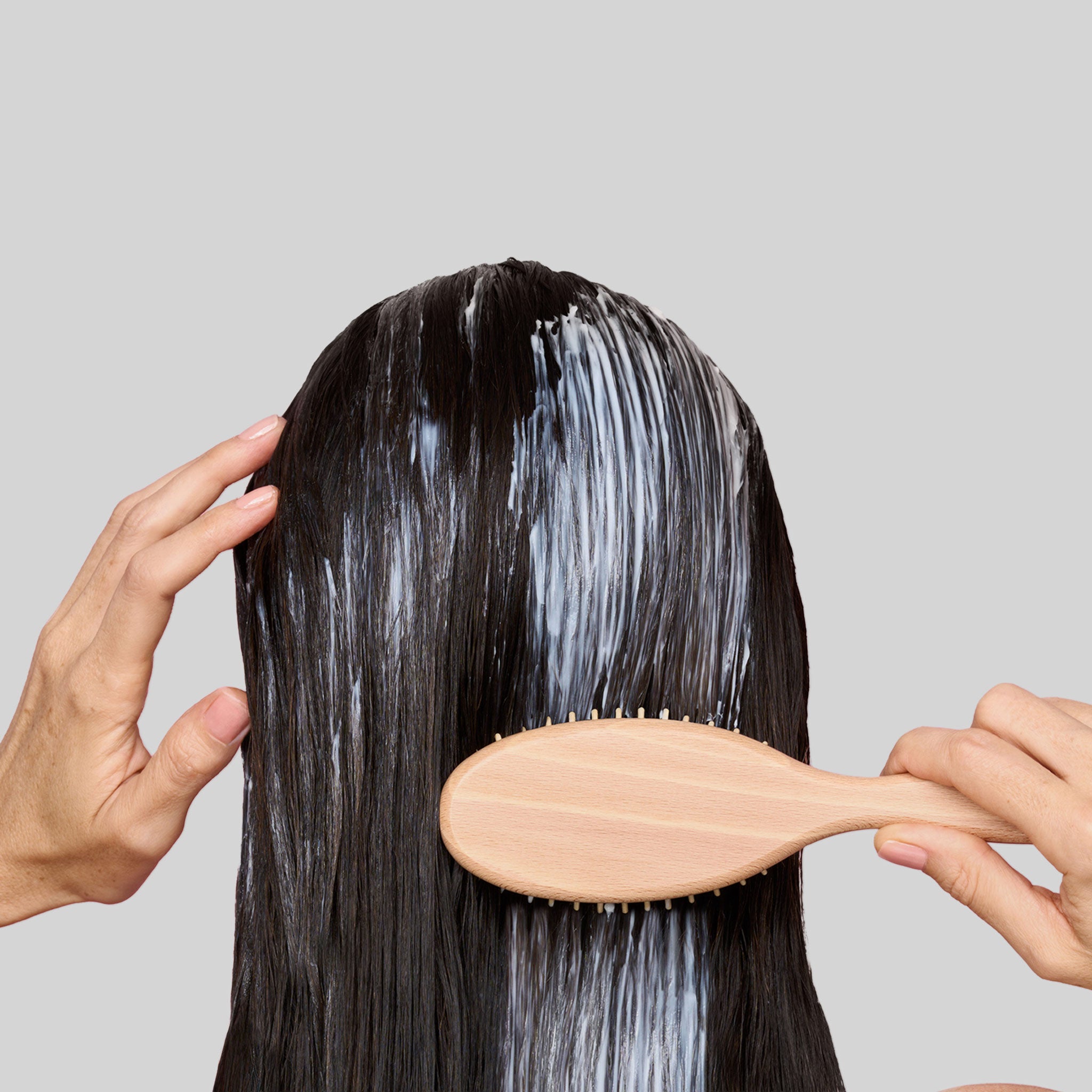 Dettaglio di capelli lunghi bagnati pettinati con un pettine in legno dopo l'applicazione del balsamo Bioscalin®