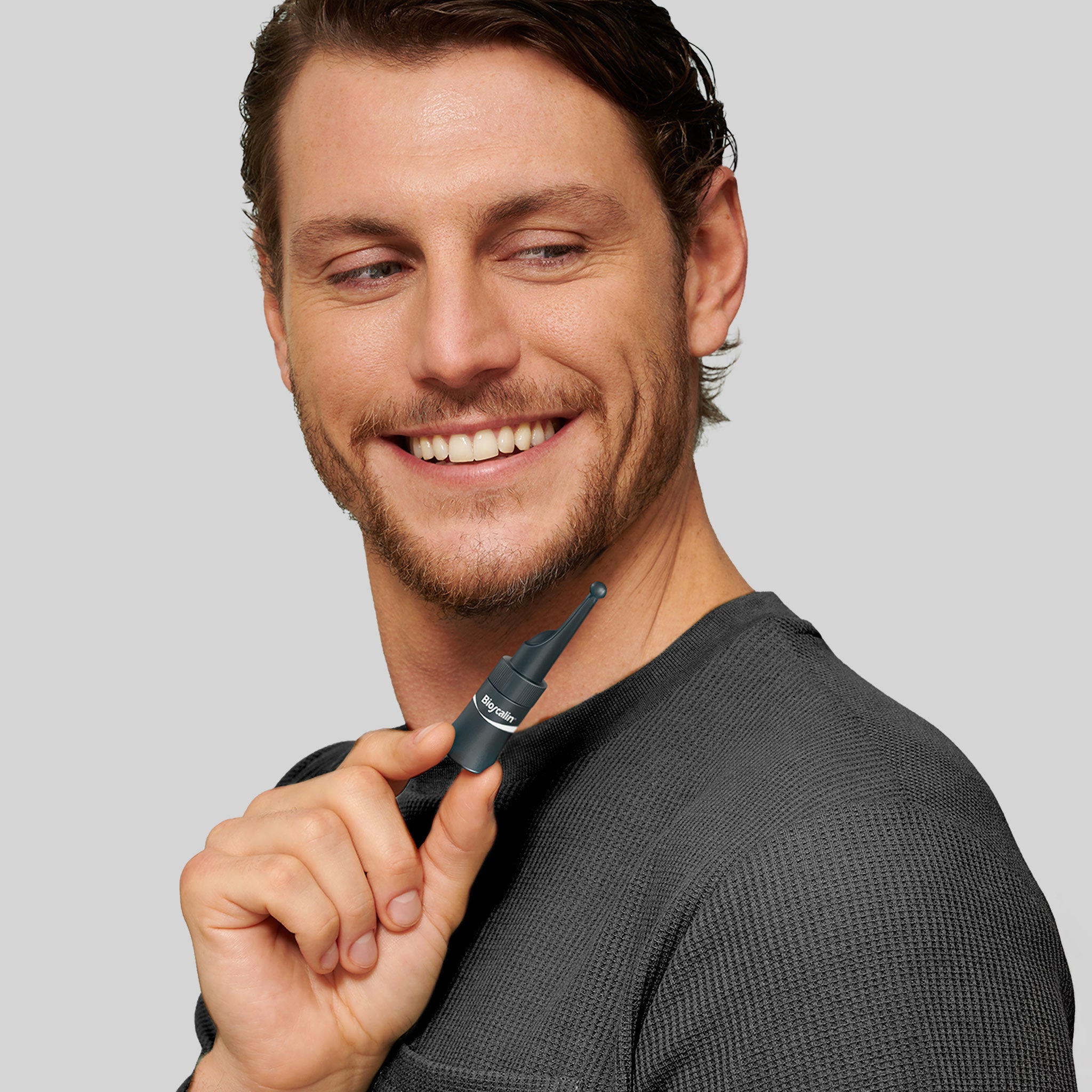 Uomo sorridente che mostra il flacone di Booster Capillare Bioscalin®