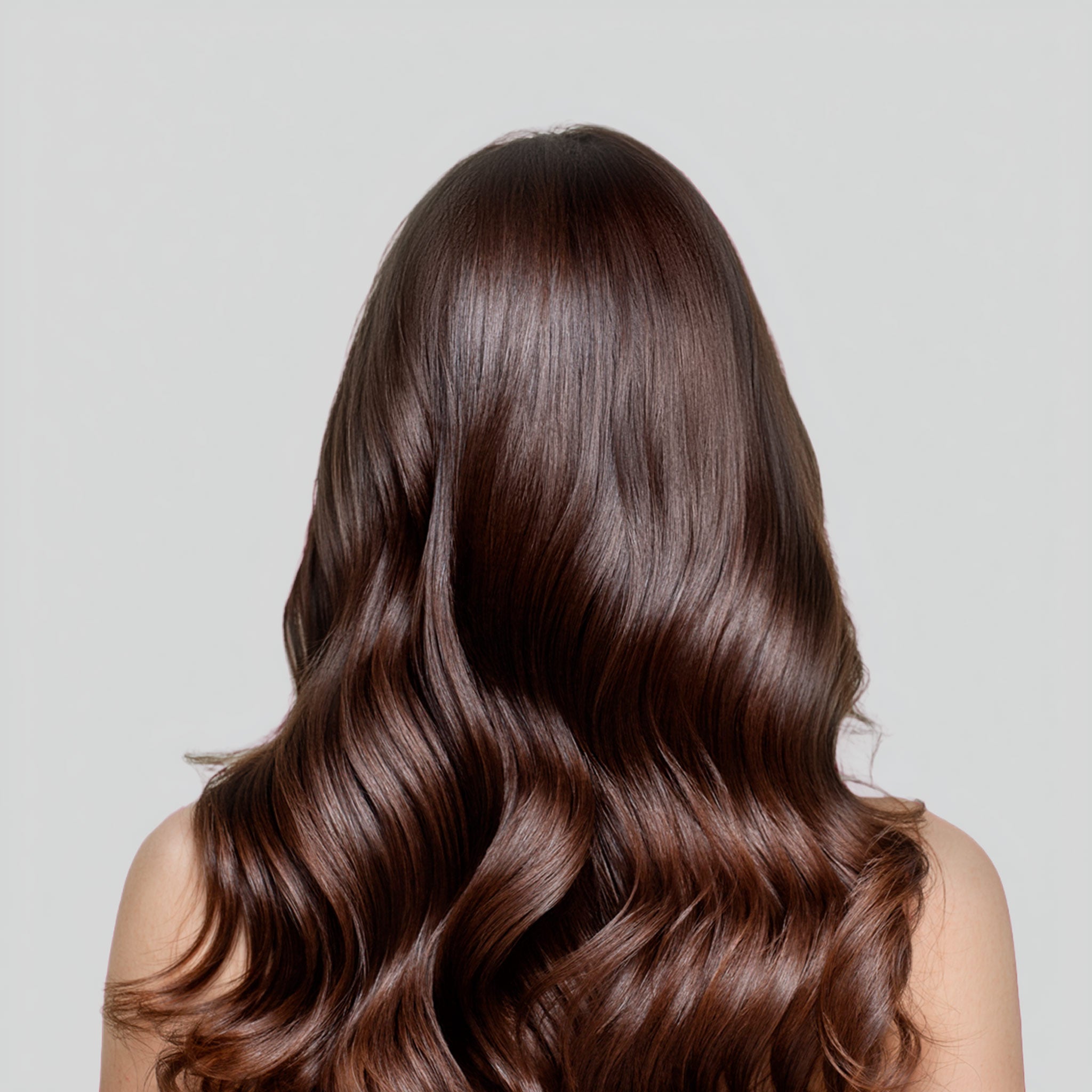 Donna che pettina i propri capelli castani e luminosi con un pettine a denti larghi dopo l'applicazione della tinta Bioscalin®